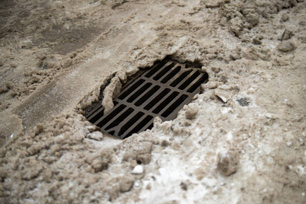 snow-melted stormwater drain on a road, symbolizing the transition from winter to spring. It highlights urban infrastructure's role in managing rainwater and melting snow