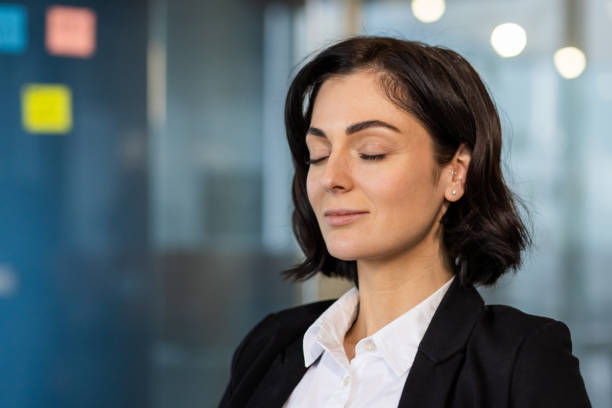 istock Woman in a professional office setting practicing mindfulness and stress relief through relaxation techniques, eyes closed, feeling peace and calm in a modern workspace environment. 2189616061