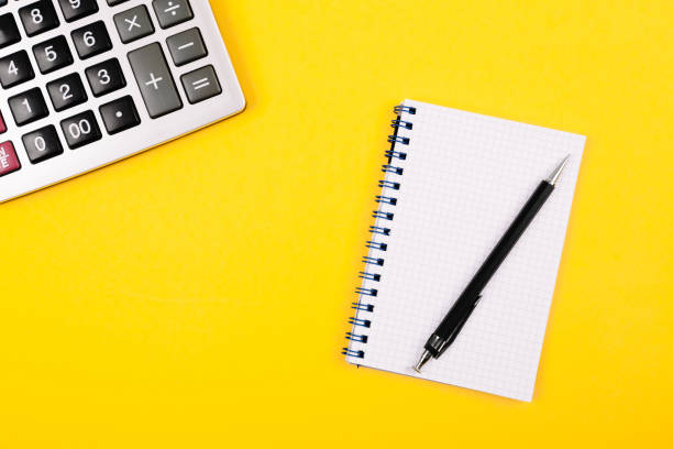istock Large silver calculator with black pen and white paper notebook on a yellow background. Conceptual photo of calculations, accounting, computing, profit, loss, tax. 2189617507