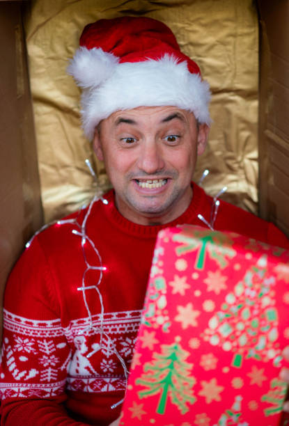 a man in red jeans is delighted with a Christmas present, he is wearing a red New Year's hat, he is enjoying himself and is happy
