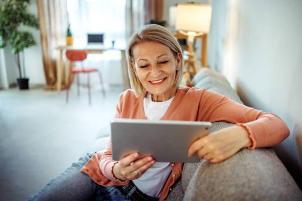 istock Mature woman using digital tablet while relaxing on a sofa at home 2189640272