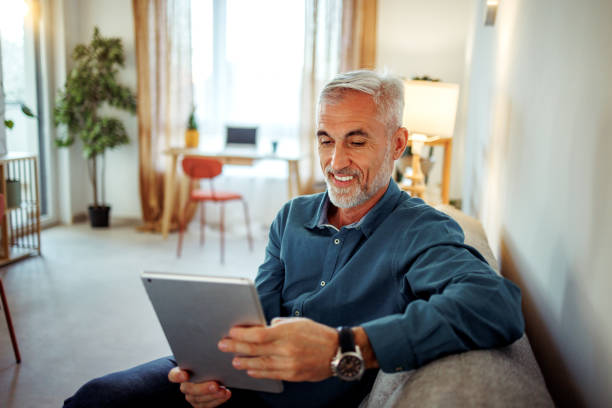 istock Casually clothed mature man using digital tablet while relaxing on a sofa at home 2189640885