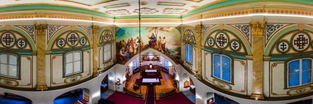 The image shows a church interior with a richly decorated ceiling, intricate patterns, and a mural above the altar. Ornate columns and stained glass are visible.