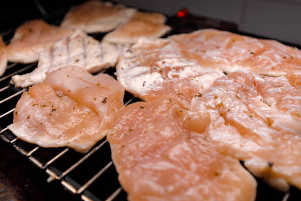 Various pieces of chicken fillets are arranged on a grill, showcasing a mix of marinated and unseasoned cuts.