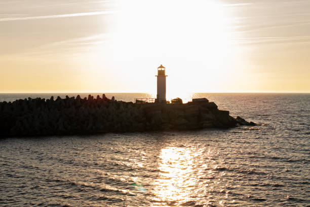 istock Lighthouse on Rocky Breakwater at Sunset with Shimmering Water 2189654737