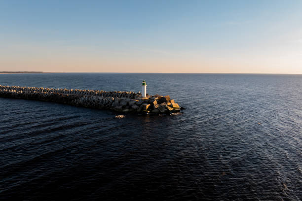 istock White Lighthouse with Green Top on Rocky Breakwater at Sunset 2189654740