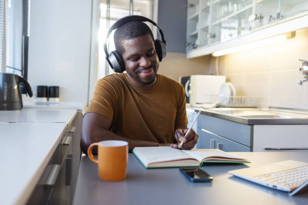 istock Man studying at home while wearing headphones and writing in a notebook 2189654950