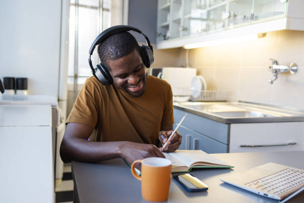 istock Man studying at home while wearing headphones and writing in a notebook 2189654953