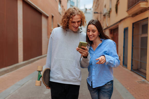 istock Young couple using smartphone and walking down the street with skateboard 2189655439