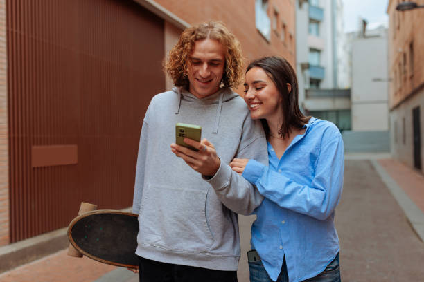 istock Young couple smiling and using smartphone outdoors 2189655460