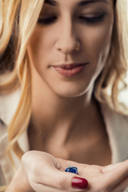 Young adult woman with blond hair and red fingernail polish looking at a tiny wrapped gift in her open hand, symbolizing joy, surprise, and the anticipation of receiving a precious present