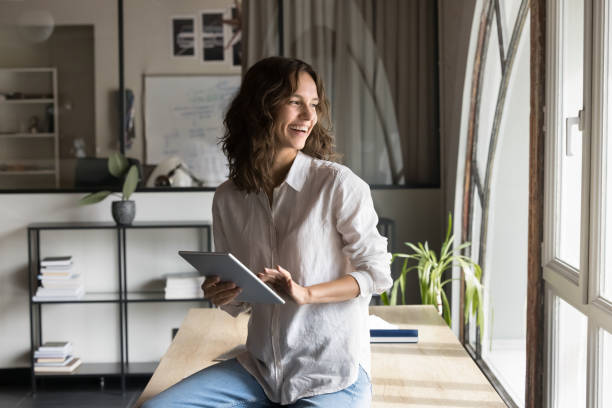 istock Pretty woman holding tablet, looking out window with smile 2189659754