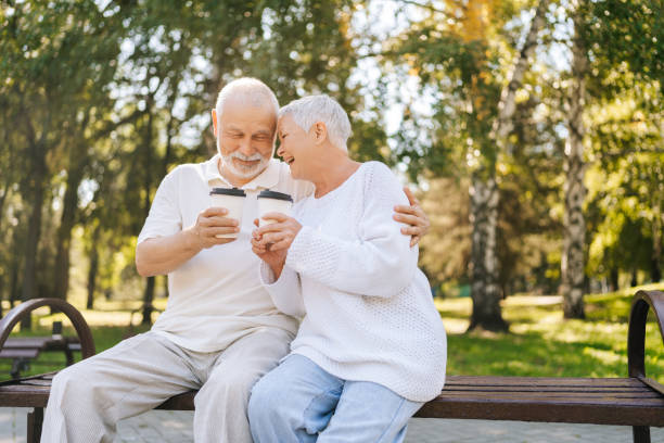 istock Loving cheerful elderly couple savoring coffee on park bench, conversing, grinning, sharing laughter under sunny trees 2189663898