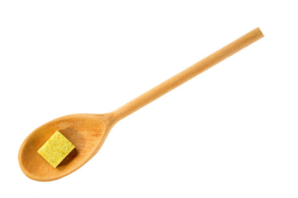 Bouillon cube in a wooden spoon isolated on a white background. Top view.