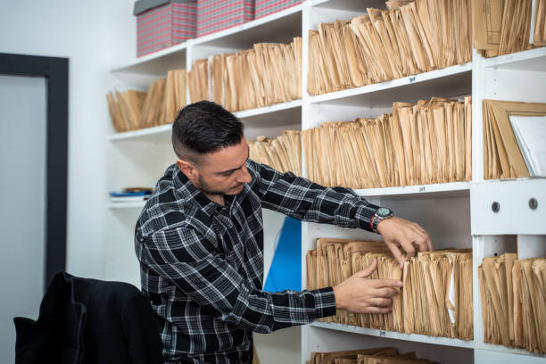 Office worker searching through files in an archive room, organizing paperwork and retrieving important documents from shelves