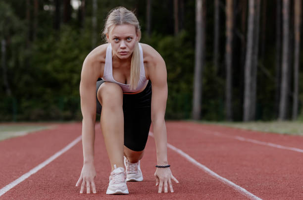 istock Fit, woman coach, athletic blonde with hair pulled back in a ponytail preparing for race run at start, doing sports, stretching at stadium, engaged against nature backdrop in summer outside 2189719657
