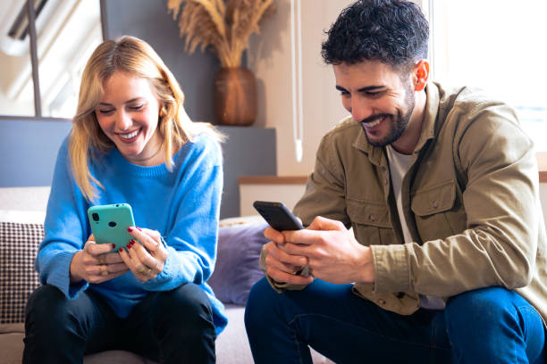 istock Joyful couple laughing while using smartphones at home, casual moment 2189727124