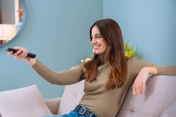 istock Woman sitting on sofa, holding remote control and smiling indoors 2189730062