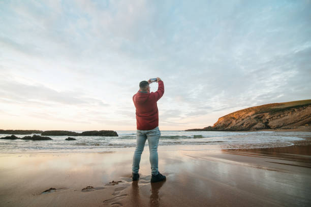 Man taking a photo of a beach at sunset using a smart phone