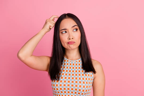 istock Thoughtful young woman scratching head against pink background, pondering decision-making. 2189746519