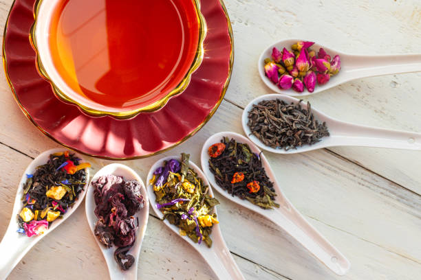 istock Assorted loose leaf teas with teacup. An elegant red teacup with loose leaf tea assortments on ceramic spoons, showcasing various herbal and floral tea blends on a rustic table. 2189747697