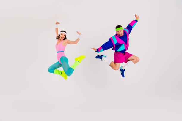 istock Energetic couple jumping in vibrant retro workout attire against a white backdrop, showcasing dynamic movement. 2189754646