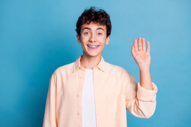 istock Joyful young man with braces waving against a blue background in casual style 2189754976