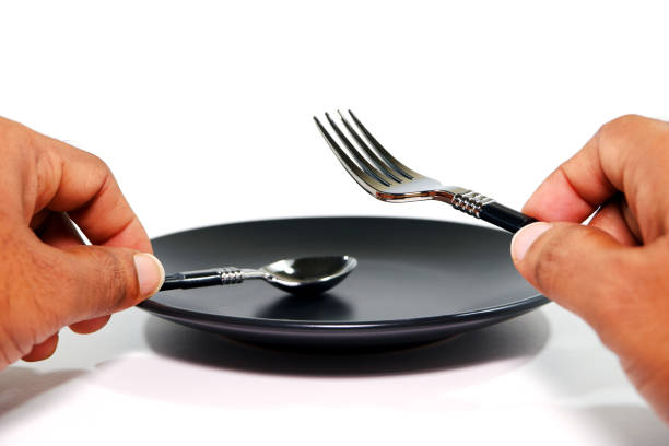istock Cutlery set holding hand before black plate with white background close-up view 2189755124