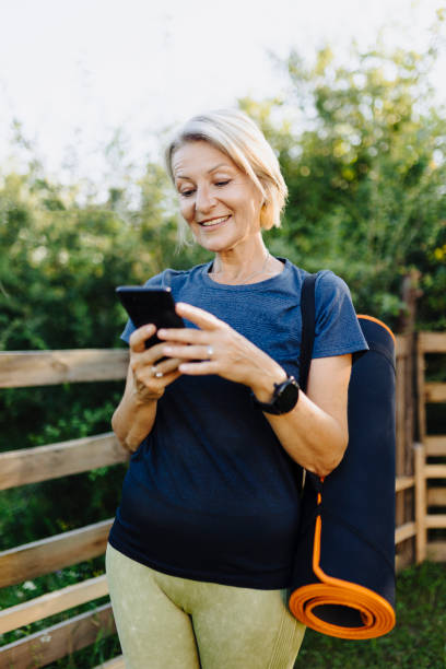 istock Senior sporty woman holding exercise mat and using smart phone 2189769206