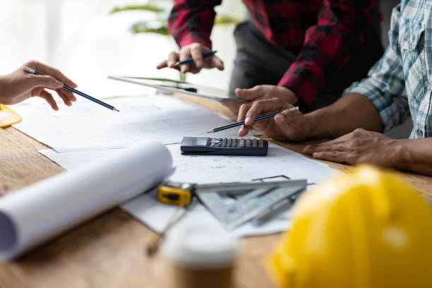 istock Brainstorming group of architects and engineers discuss building blueprint design paperwork and drawing construction project planning on wooden table in office. Construction project budget planning. 2189771491