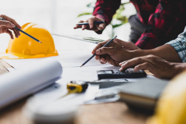 istock Brainstorming group of architects and engineers discuss building blueprint design paperwork and drawing construction project planning on wooden table in office. Construction project budget planning. 2189771492
