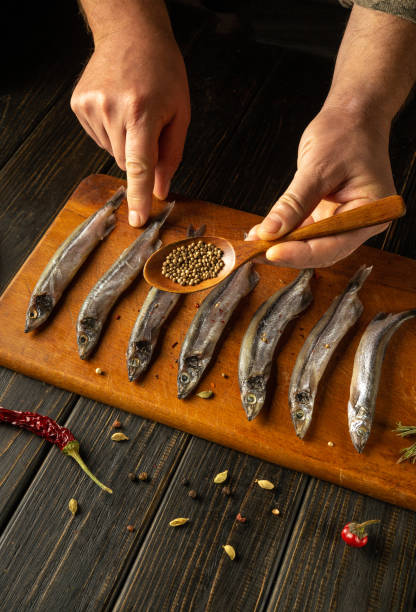 istock Skilled hands delicately arrange fresh fish on a wooden board, expertly adding spices from a small spoon while vibrant chilies and herbs enhance the culinary atmosphere. 2189772861