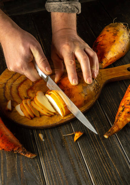istock Hands skillfully slice vibrant sweet beetroot on a beautifully grained wooden board. The warm tones of the kitchen create an inviting atmosphere for cooking 2189772869
