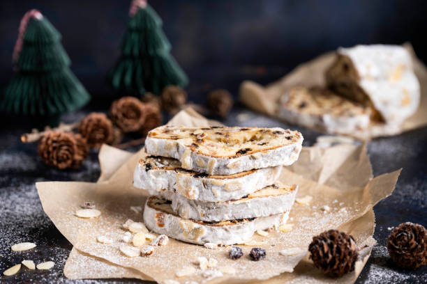 Sliced German Christmas fruit cake known as Stollen cake on parchment paper. There are Christmas decorations in the background.