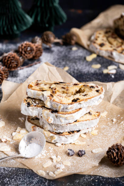 Sliced German Christmas fruit cake known as Stollen cake on parchment paper. There are Christmas decorations in the background.