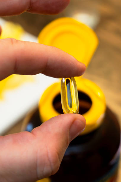 istock Hand holding a golden supplement capsule above an open bottle 2189779784