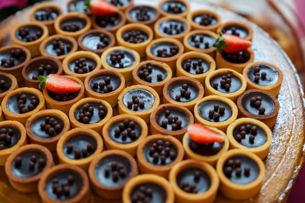Close-up shot of delicious chocolate tartlets topped with chocolate balls and garnished with fresh strawberries. The crisp tart shells are filled with creamy chocolate filling, making these bite-sized desserts both visually appealing and irresistibly tasty.