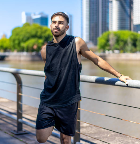 Athletic male warming up with stretches by the urban waterfront