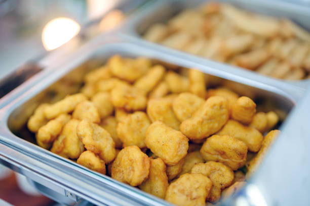 Buffet meal served with a large tray of crispy golden fried chicken nuggets on a serving dish, perfect for catering events and gatherings. The background shows more dishes in a buffet setting.