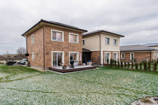 A brick house with a patio and a driveway. The house is surrounded by a snow-covered yard. Two adjacent two-story houses with brick facades and plaster exterior, complemented by a snowy green lawn