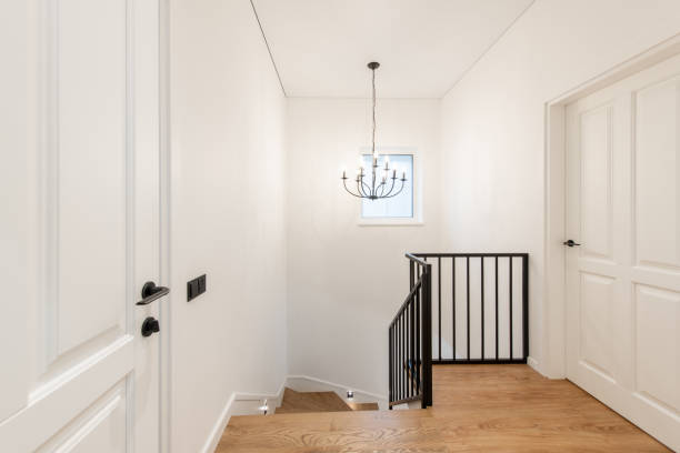Bright Home House Hallway with Wooden Flooring and Modern Black Staircase Design A minimalistic modern home, house hallway featuring warm wooden flooring, elegant black railed staircase, white panel doors, illuminated by a contemporary metal chandelier. stairwell chandelier stock pictures, royalty-free photos & images