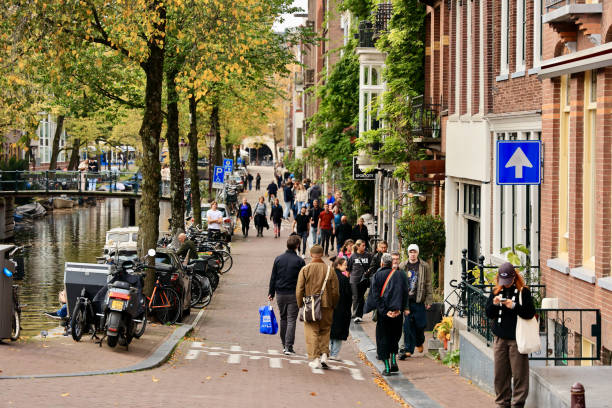 People are walking past the historic old canal houses in the center of Amsterdam.