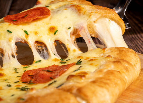 Close-up of server lifting a slice of pepperoni pizza, showcasing melted cheese stretching from the rest of the pie