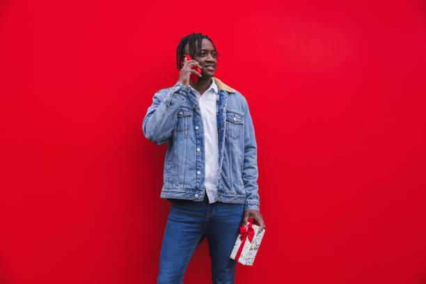 istock Young man talking on the phone and holding a gift on red background. 2189795158