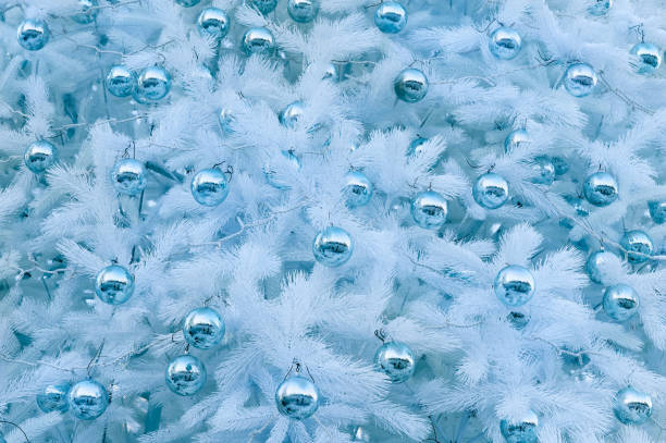 White Christmas trees stand side by side, adorned with shiny blue and silver ornaments, creating a festive atmosphere in a contemporary indoor setting