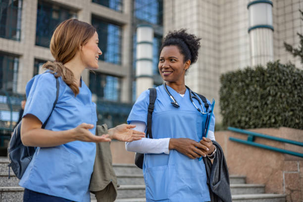 Two multiracial female healthcare professionals, one Black and the other White, are seen walking toward the hospital entrance, ready to start their shift. The image emphasizes the importance of diversity in the healthcare industry, where professionals from different backgrounds come together to deliver quality care. Their confident expressions and teamwork reflect the dedication and commitment required in the medical field, while the hospital backdrop symbolizes a place of healing and innovation.