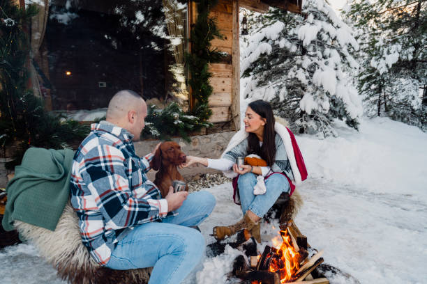 istock Couple with dog siting around fire pit in front of the cabin 2189827176
