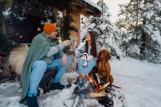 istock Couple with dog siting around fire pit in front of the cabin 2189827249