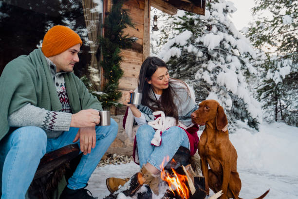istock Couple with dog siting around fire pit in front of the cabin 2189827250