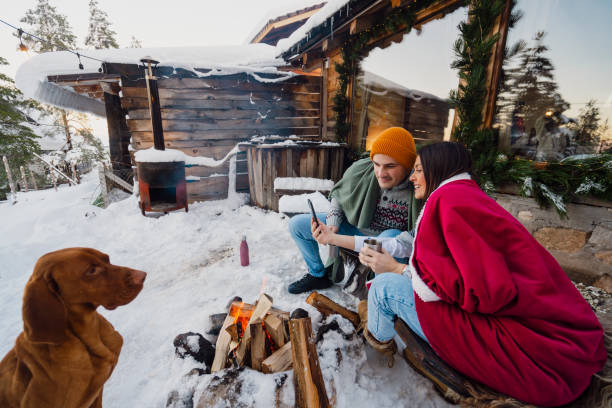 istock Couple with dog siting around fire pit in front of the cabin 2189827252
